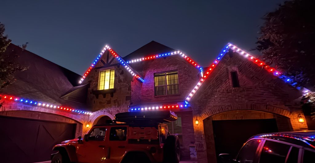Front of a home at dark with bright red white and blue LEDs along the rooflines